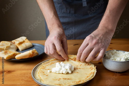 A man in the kitchen prepares a healthy breakfast of pancakes stuffed with fresh cottage cheese with sour cream and delicious fragrant honey.