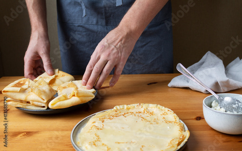 A man in the kitchen prepares a healthy breakfast of pancakes stuffed with fresh cottage cheese with sour cream and delicious fragrant honey.