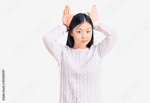 Young beautiful chinese woman wearing casual sweater doing bunny ears gesture with hands palms looking cynical and skeptical. easter rabbit concept.