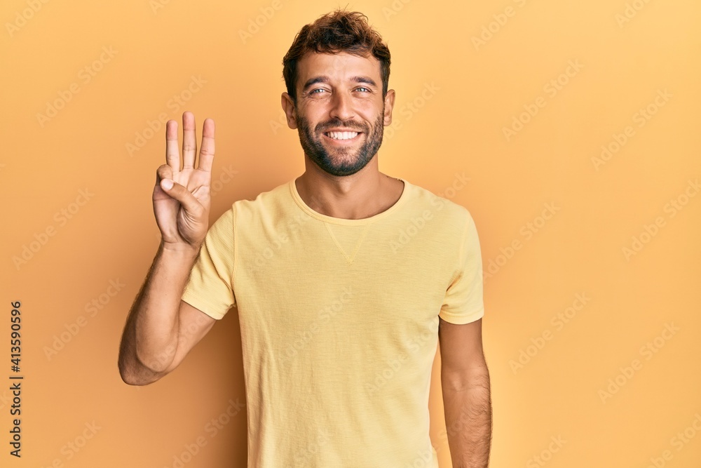 Handsome man with beard wearing casual yellow tshirt over yellow background showing and pointing up with fingers number three while smiling confident and happy. Handsome man with beard wearing casual yellow tshirt over yellow background showing and pointing up with fingers number three while smiling confident and happy.