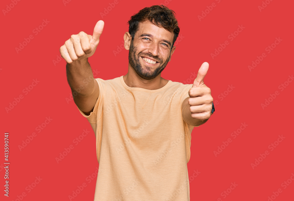 Handsome young man with beard wearing casual tshirt approving doing positive gesture with hand, thumbs up smiling and happy for success. winner gesture. Handsome young man with beard wearing casual tshirt approving doing positive gesture with hand, thumbs up smiling and happy for success. winner gesture.