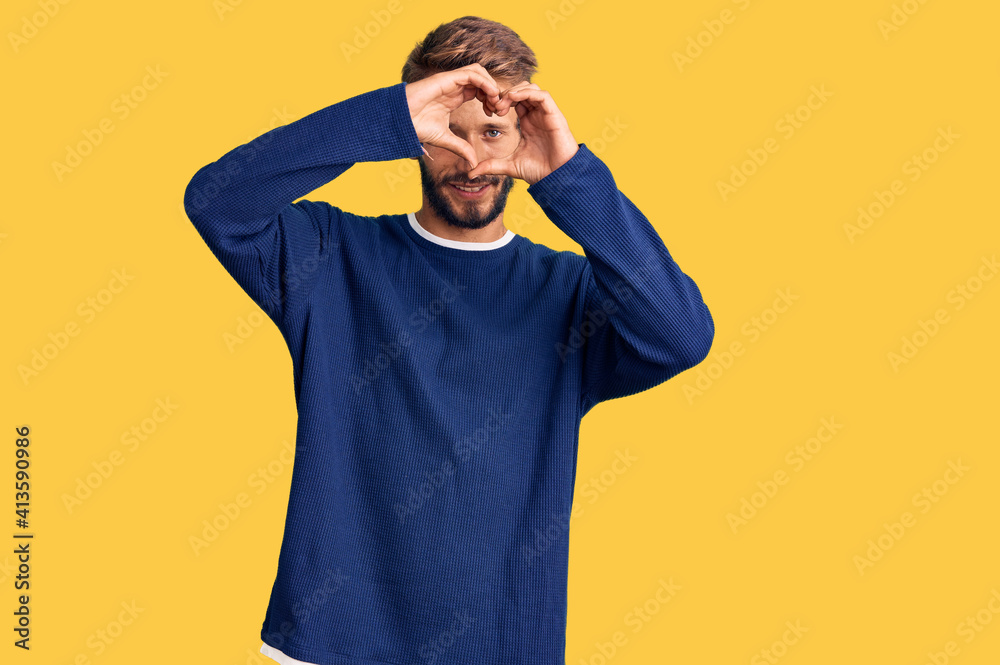 Handsome blond man with beard wearing casual sweater doing heart shape with hand and fingers smiling looking through sign Handsome blond man with beard wearing casual sweater doing heart shape with hand and fingers smiling looking through sign