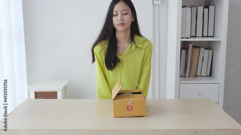 Young asian woman walking and unpacking of parcel box with online shopping while satisfied at home, female opening package with purchase for online store and looking with excited, delivery concept. Young asian woman walking and unpacking of parcel box with online shopping while satisfied at home, female opening package with purchase for online store and looking with excited, delivery concept.