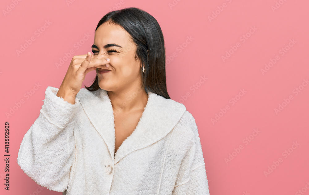 Young brunette woman wearing casual clothes smelling something stinky and disgusting, intolerable smell, holding breath with fingers on nose. bad smell Young brunette woman wearing casual clothes smelling something stinky and disgusting, intolerable smell, holding breath with fingers on nose. bad smell