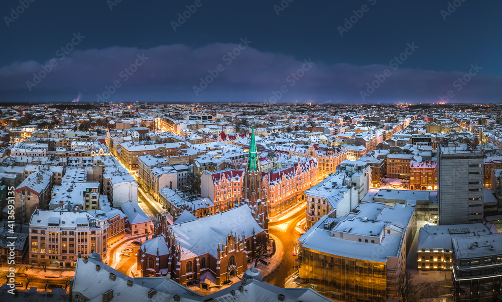 Riga city panorama in winter time. Street lights glowing in blue hour. Snowy rooftops. Iconic buildings and architecture. Drone footage.