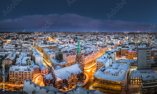 Obraz na płótnie Riga city panorama in winter time. Street lights glowing in blue hour. Snowy rooftops. Iconic buildings and architecture. Drone footage. w salonie