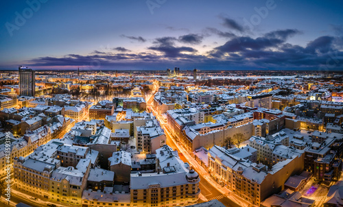 Riga city panorama in winter time. Street lights glowing in blue hour. Snowy rooftops. Iconic buildings and architecture. Drone footage.  © Viesturs