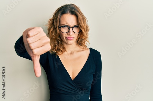 Young caucasian woman wearing business shirt and glasses looking unhappy and angry showing rejection and negative with thumbs down gesture. bad expression.