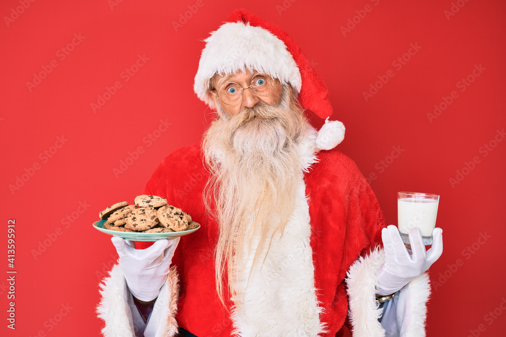 Φωτογραφία Old senior man with grey hair and long beard wearing santa claus costume holding cookies and milk clueless and confused expression