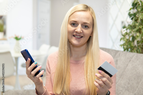 Blonde girl sit on the couch with phone and credit card. concept online shopping