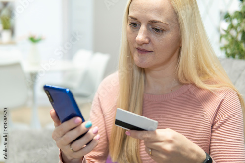 Blonde girl sit on the couch with phone and credit card. concept online shopping