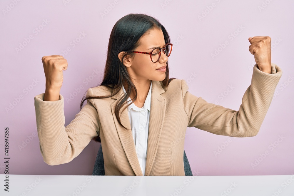 Beautiful hispanic woman working at the office showing arms muscles smiling proud. fitness concept. Beautiful hispanic woman working at the office showing arms muscles smiling proud. fitness concept.