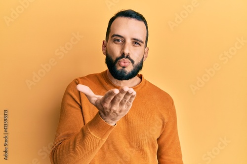 Young man with beard wearing casual winter sweater looking at the camera blowing a kiss with hand on air being lovely and sexy. love expression.