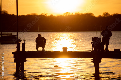 Silhouette of people fishing off of a dock or pier during sunset golden hour or sunrise