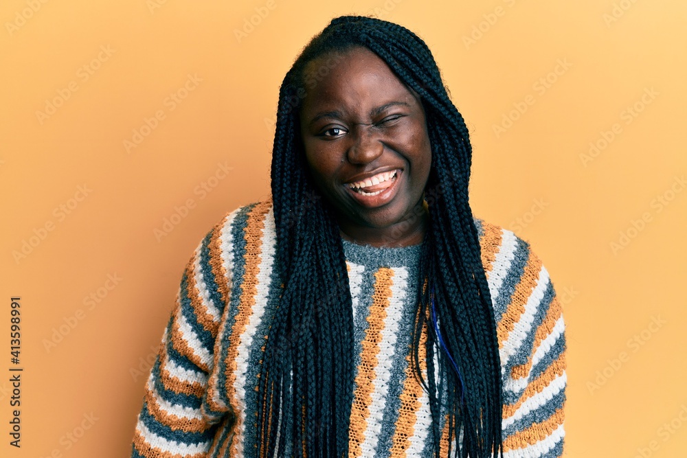 Young black woman with braids wearing casual winter sweater winking looking at the camera with sexy expression, cheerful and happy face. Young black woman with braids wearing casual winter sweater winking looking at the camera with sexy expression, cheerful and happy face.