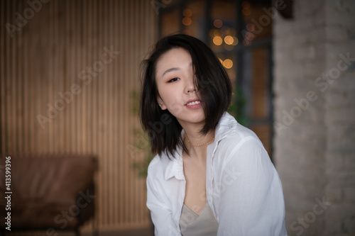 Portrait of a beautiful Asian young woman in a white fashionable shirt at home in a dark loft design interior.