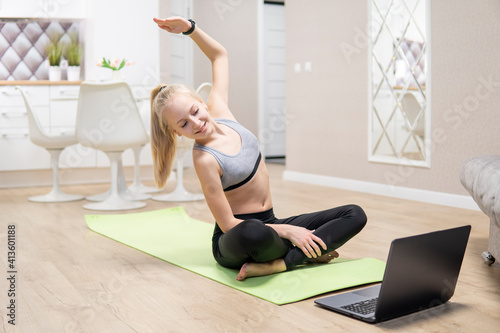 young attractive girl is engaged in fitness at home and looks at the laptop. quarantine fitness concept