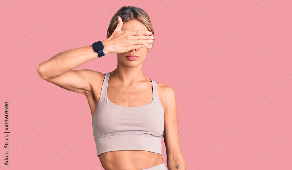 Beautiful caucasian woman wearing sportswear covering eyes with hand, looking serious and sad. sightless, hiding and rejection concept Beautiful caucasian woman wearing sportswear covering eyes with hand, looking serious and sad. sightless, hiding and rejection concept