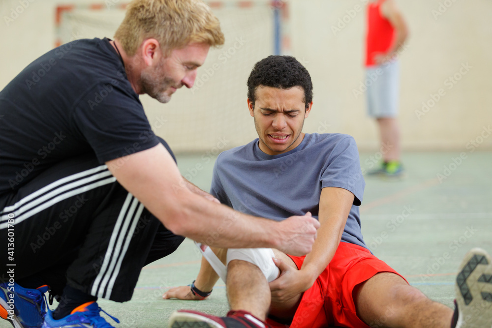 Obraz premium coach bandaging the knee of injured young sportsman