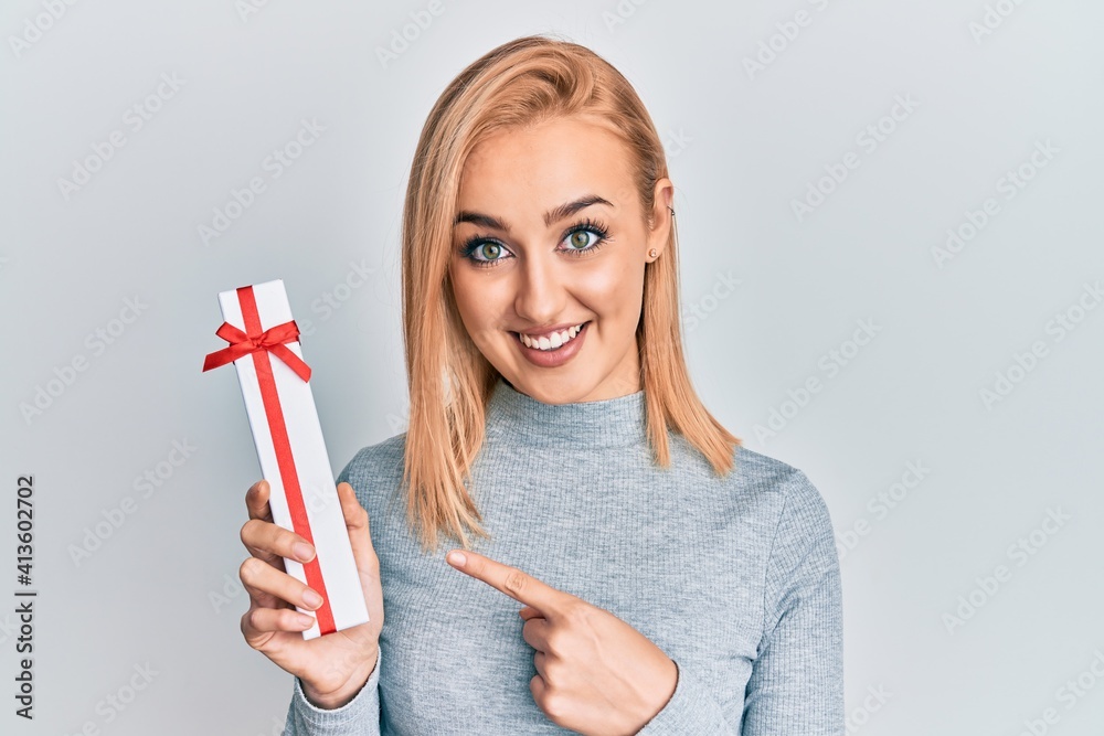 Beautiful caucasian woman holding gift smiling happy pointing with hand and finger Beautiful caucasian woman holding gift smiling happy pointing with hand and finger