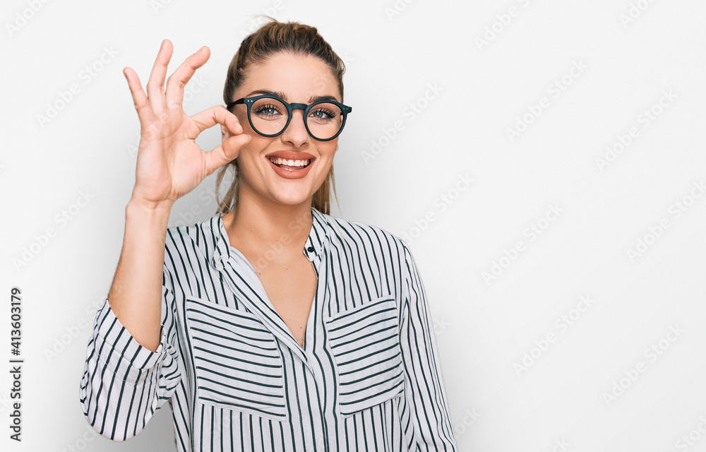 Young caucasian woman wearing business shirt and glasses smiling positive doing ok sign with hand and fingers. successful expression.