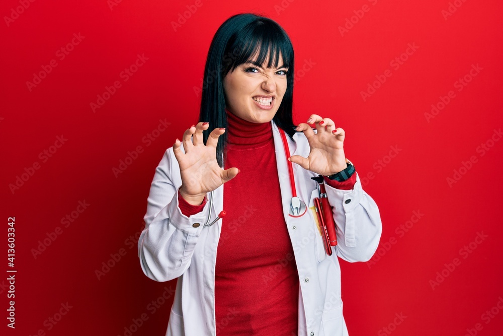 Young hispanic woman wearing doctor uniform and stethoscope smiling funny doing claw gesture as cat, aggressive and sexy expression Young hispanic woman wearing doctor uniform and stethoscope smiling funny doing claw gesture as cat, aggressive and sexy expression