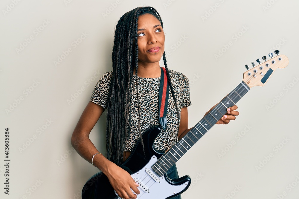 African american woman playing electric guitar smiling looking to the side and staring away thinking. African american woman playing electric guitar smiling looking to the side and staring away thinking.
