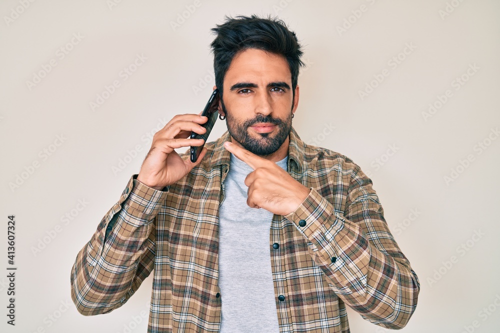 Handsome hispanic man with beard having conversation talking on the smartphone relaxed with serious expression on face. simple and natural looking at the camera. Handsome hispanic man with beard having conversation talking on the smartphone relaxed with serious expression on face. simple and natural looking at the camera.