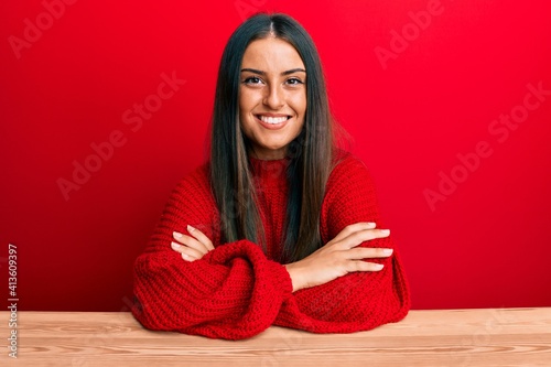 Beautiful hispanic woman wearing casual clothes sitting on the table happy face smiling with crossed arms looking at the camera. positive person. photo