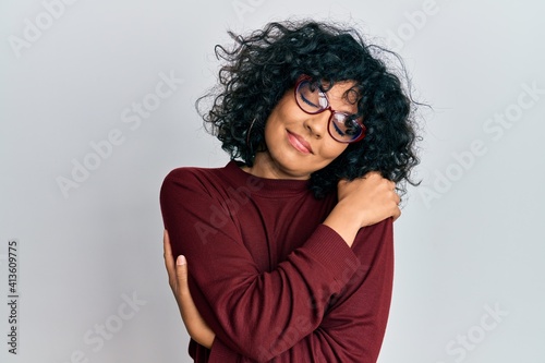 Young hispanic woman wearing casual clothes and glasses hugging oneself happy and positive, smiling confident. self love and self care