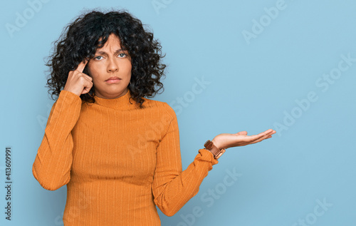 Young hispanic woman wearing casual clothes confused and annoyed with open palm showing copy space and pointing finger to forehead. think about it.