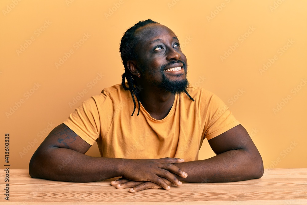 Handsome young black man wearing casual clothes sitting on the table looking away to side with smile on face, natural expression. laughing confident. Handsome young black man wearing casual clothes sitting on the table looking away to side with smile on face, natural expression. laughing confident.