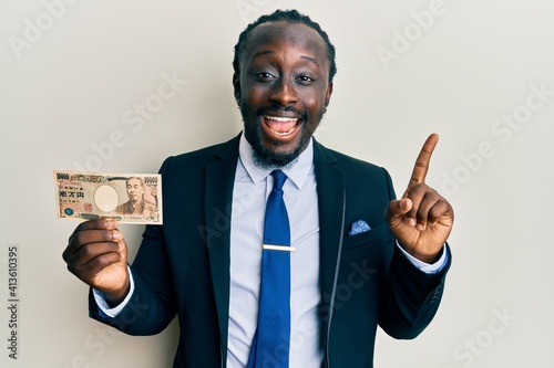 Handsome young black man wearing business suit holding 1000 yen banknotes smiling happy pointing with hand and finger to the side