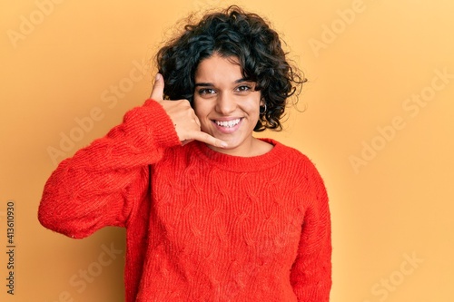Young hispanic woman with curly hair wearing casual winter sweater smiling doing phone gesture with hand and fingers like talking on the telephone. communicating concepts. © Krakenimages.com