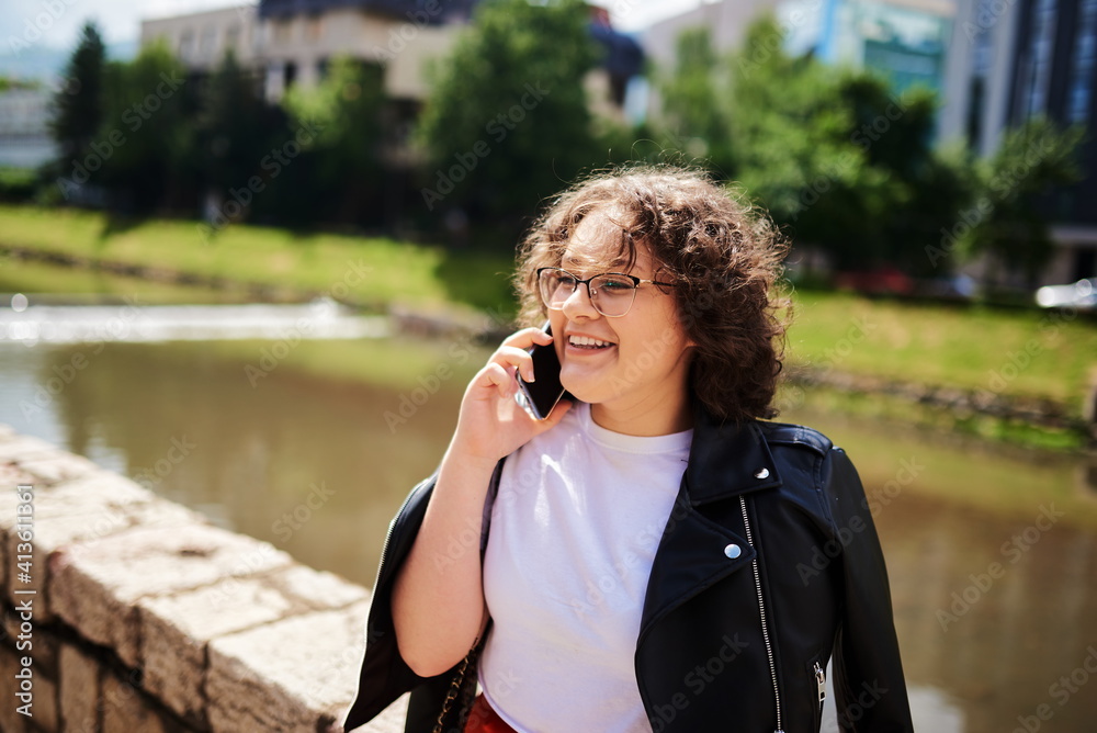 Smiling curly woman wearing trendy sunglasses walks down the central city street and uses her phone. Smiling curly woman wearing trendy sunglasses walks down the central city street and uses her phone.