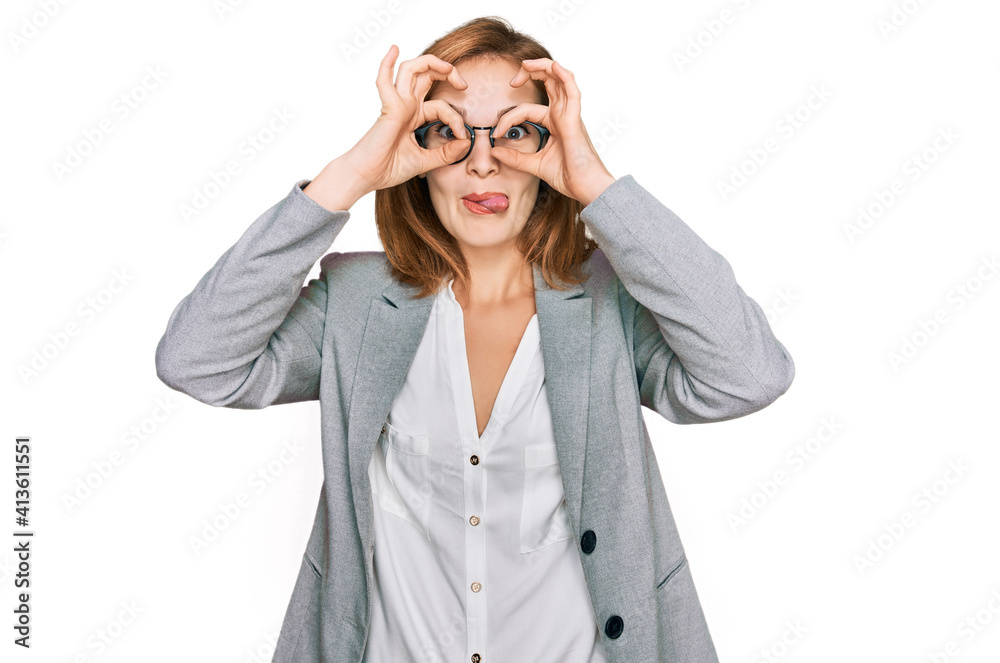 Young caucasian woman wearing business style and glasses doing ok gesture like binoculars sticking tongue out, eyes looking through fingers. crazy expression. Young caucasian woman wearing business style and glasses doing ok gesture like binoculars sticking tongue out, eyes looking through fingers. crazy expression.