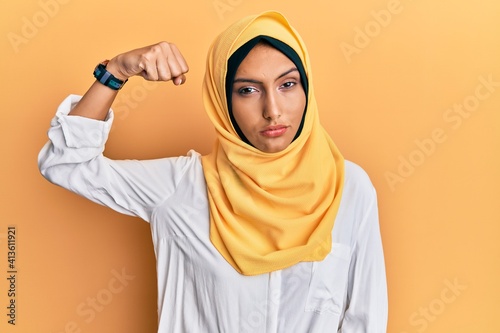 Young brunette arab woman wearing traditional islamic hijab scarf strong person showing arm muscle, confident and proud of power © Krakenimages.com