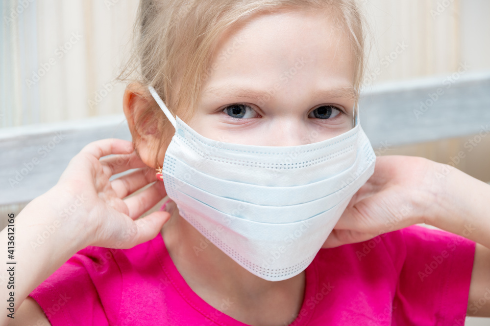 Caucasian little girl puts on a disposable hygienic mask to protect against the spread of the disease, close-up. Preventing the Spread of COVID-19 Virus, Common Cold Flu, or Environmental Pollution