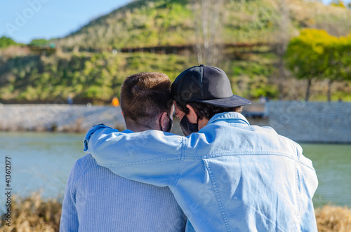 nClose Up of Gay Couple Back with Protective Mask Embracing and Hugging Each Other In front of Lake Park photo