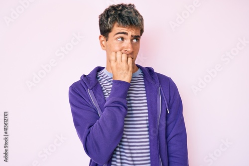 Young handsome man wearing casual purple sweatshirt looking stressed and nervous with hands on mouth biting nails. anxiety problem.
