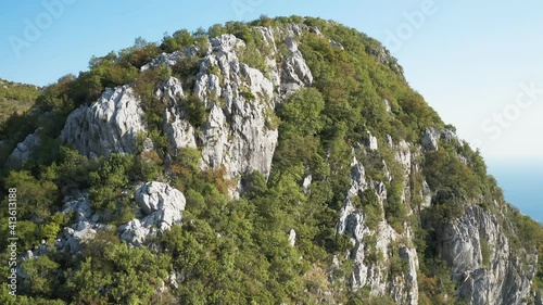 Rock formation.Unique natural landscape.Green bushes and trees grow on the flat gray rock at the top of the cliff. Top view from drone. Mount Chelobrdo above Budva.
 photo