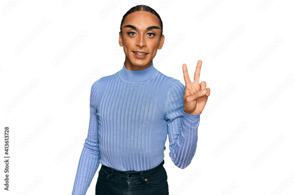 Hispanic transgender man wearing make up and long hair wearing casual clothes smiling with happy face winking at the camera doing victory sign. number two. Hispanic transgender man wearing make up and long hair wearing casual clothes smiling with happy face winking at the camera doing victory sign. number two.
