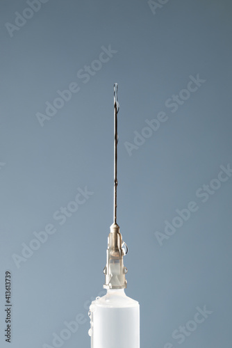 A jet and drops of medicine on a syringe needle on a gray background. Medicine concept, vaccination. Close up, copy space