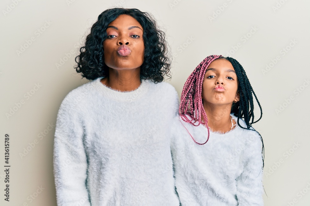 Beautiful african american mother and daughter wearing casual winter sweater looking at the camera blowing a kiss on air being lovely and sexy. love expression. Beautiful african american mother and daughter wearing casual winter sweater looking at the camera blowing a kiss on air being lovely and sexy. love expression.