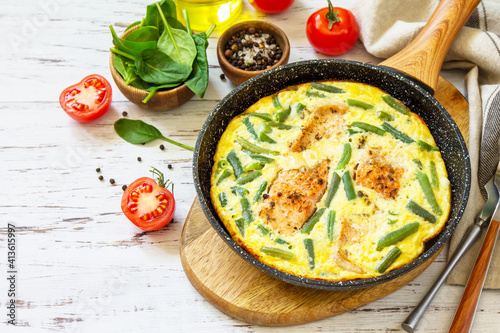 Healthy breakfast or diet lunch. Rustic omelet (omelette, Scrambled) with salmon fillet and green beans in a cast iron pan on a white kitchen wooden table. Copy space.