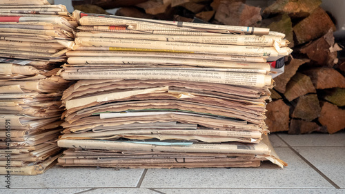 Ein stapel mit Altpapier aus alten Zeitungen vor einem Holzstapel