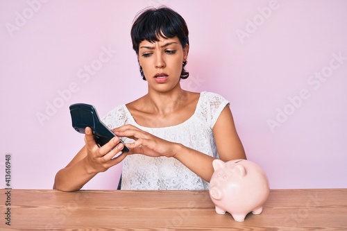 Beautiful brunettte woman caculating money savings clueless and confused expression. doubt concept. photo