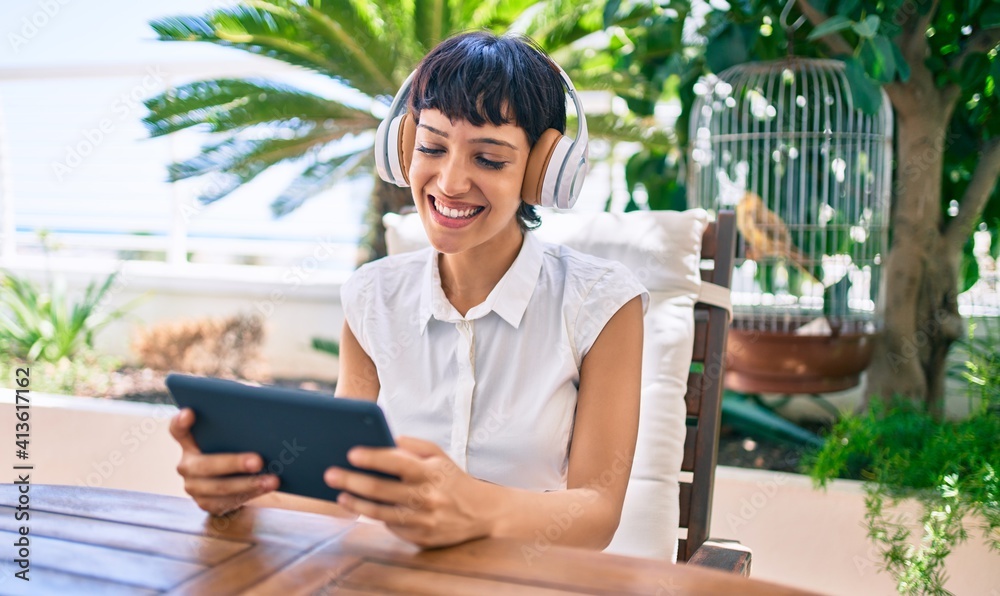 Beautiful woman with short hair sitting at the terrace on a sunny day wearing headphones using touchpad device Beautiful woman with short hair sitting at the terrace on a sunny day wearing headphones using touchpad device