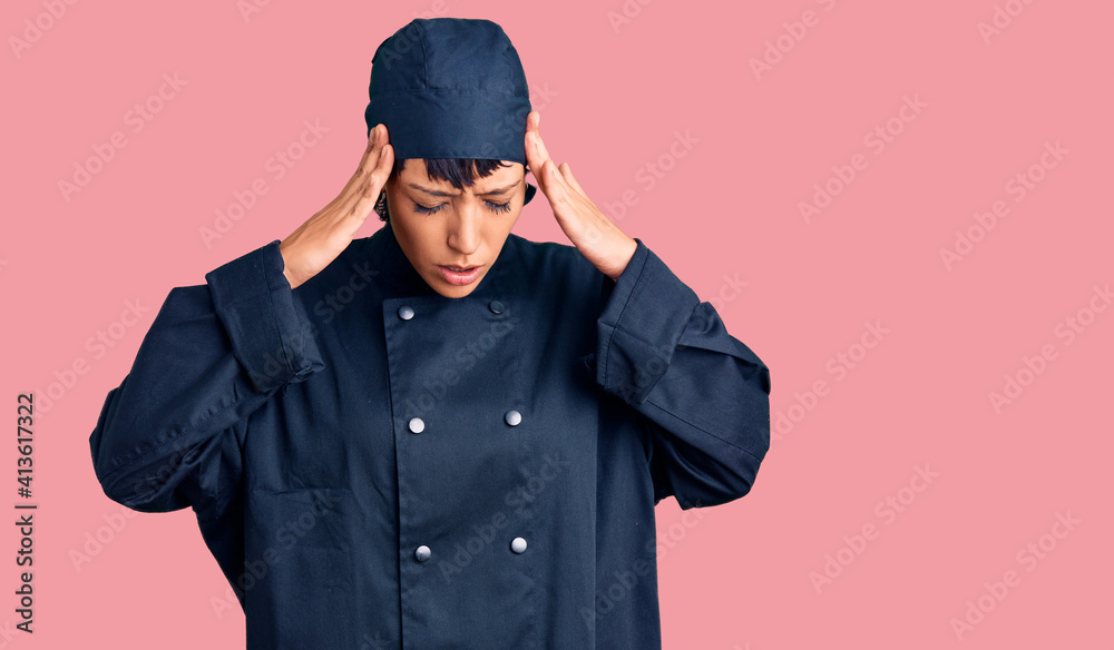 Young brunette woman with short hair wearing professional cook uniform with hand on head for pain in head because stress. suffering migraine.