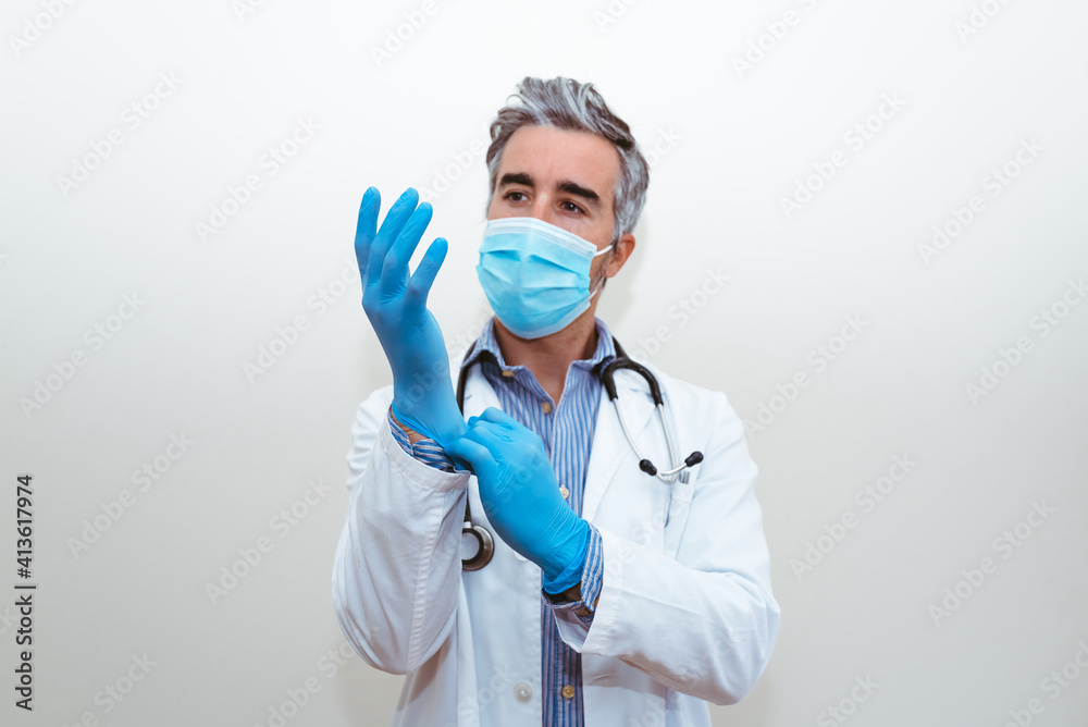 Doctor with mask in uniform putting on gloves with a white background Doctor with mask in uniform putting on gloves with a white background